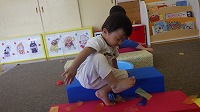 足の裏に付いたすずらんテープを積み木に座って取ろうとしている男の子
