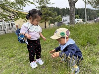 公園で何かを見つけてしゃがみ込んでいるお友達を見ている