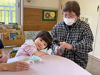 おばあさんに給食を食べさせてもらっている子ども