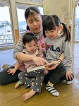 先生の膝の上で絵本を見る女の子2人