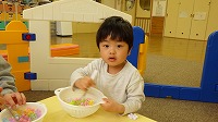 ザルに食べ物に見立てたフラワーブロックを入れかき混ぜている男の子を