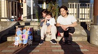 花の前でお母さんに抱っこされる女の子とお父さん